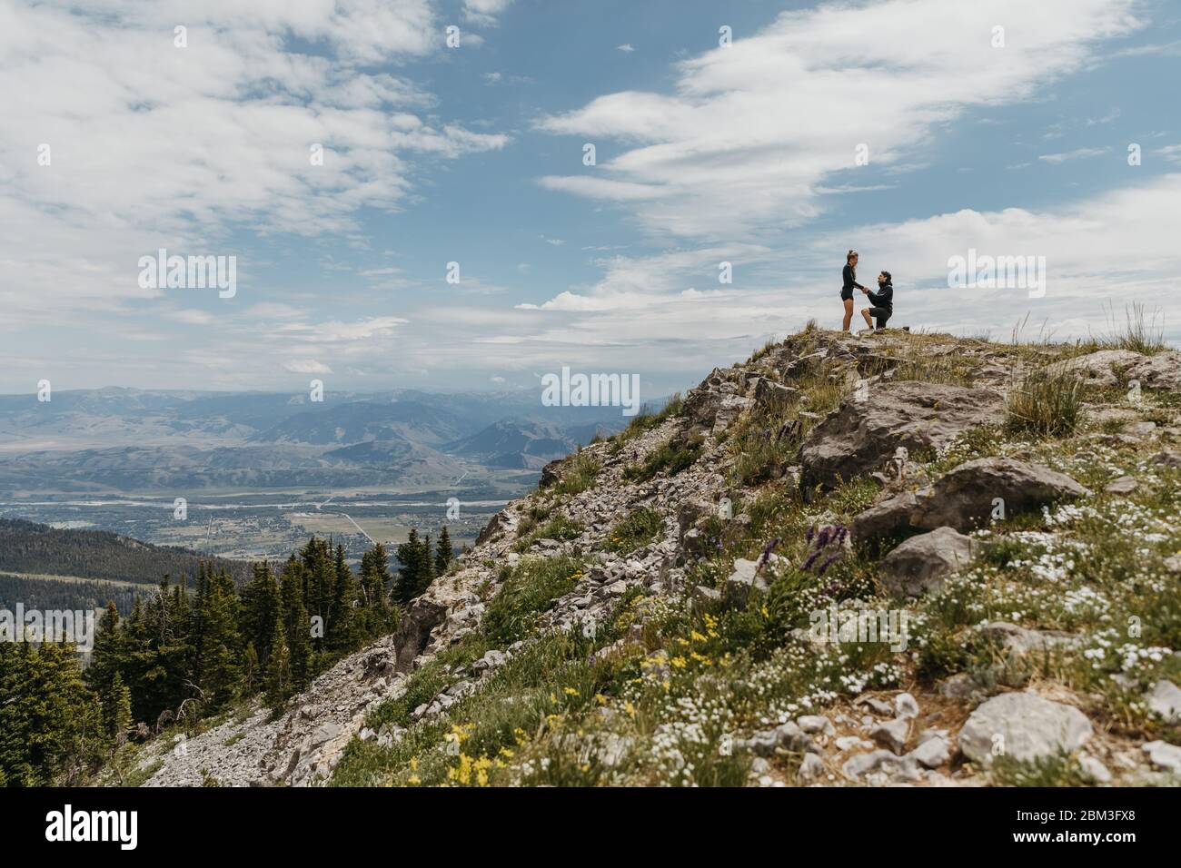 boyfriend gets down on one knee and proposes on mountain in wyoming Stock Photo