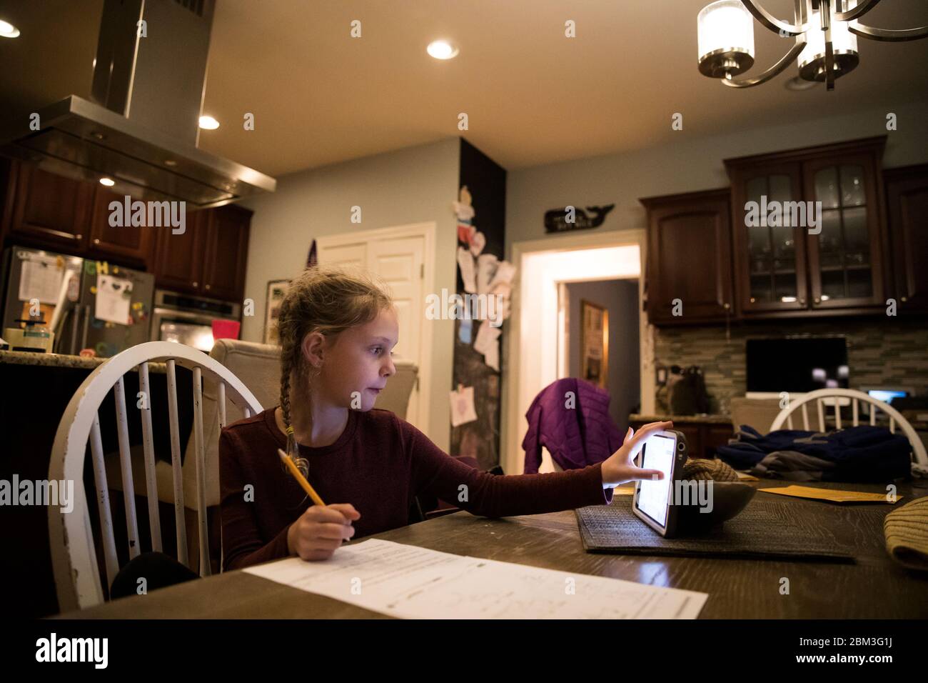 Blonde Girl at Kitchen Table Does School Work on Tablet Computer Stock Photo