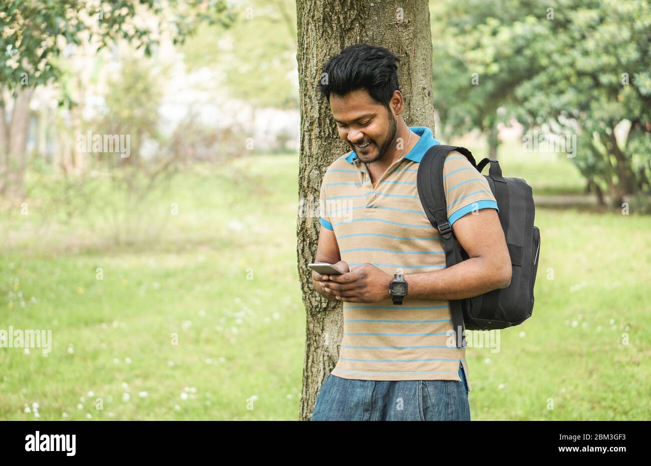 Young indian man using smartphone app in university campis - Happy asian guy having fun watching videos on mobile cell phone - Technology and millenni Stock Photo