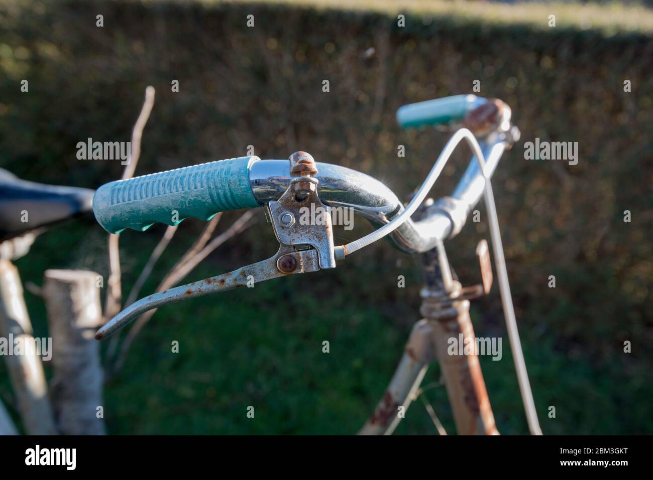 A side on close up image of an old rusting set of bicycle handlebars, hand brake and bell in afternoon sun Stock Photo
