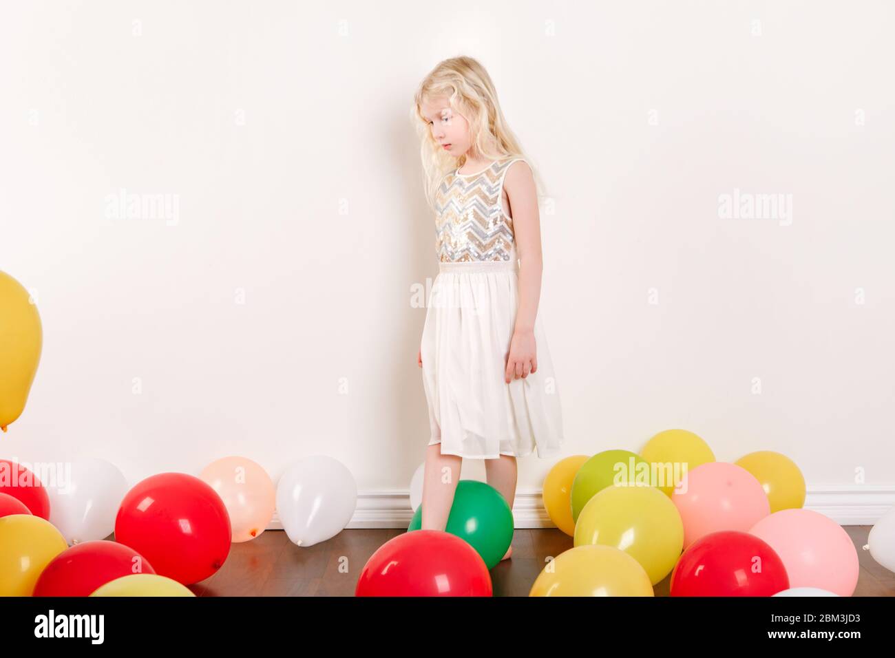 Sad upset little girl celebrating birthday at home. Lovely lonely unhappy girl child with colorful balloons. Quarantine birthday party at home alone d Stock Photo