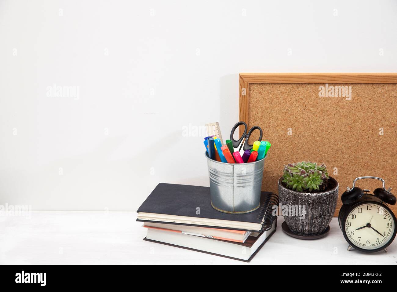 Copy space. Workplace office worker. Alarm clock, succulent in ceramic pot, writing board, bucket with scissors, felt-tip pens, ruler, three notebooks Stock Photo