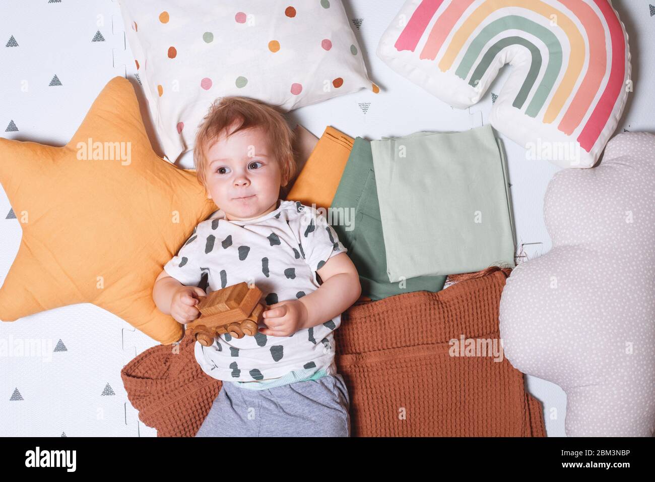Happy baby boy playing with a wooden toy car lying on the floor in the ...