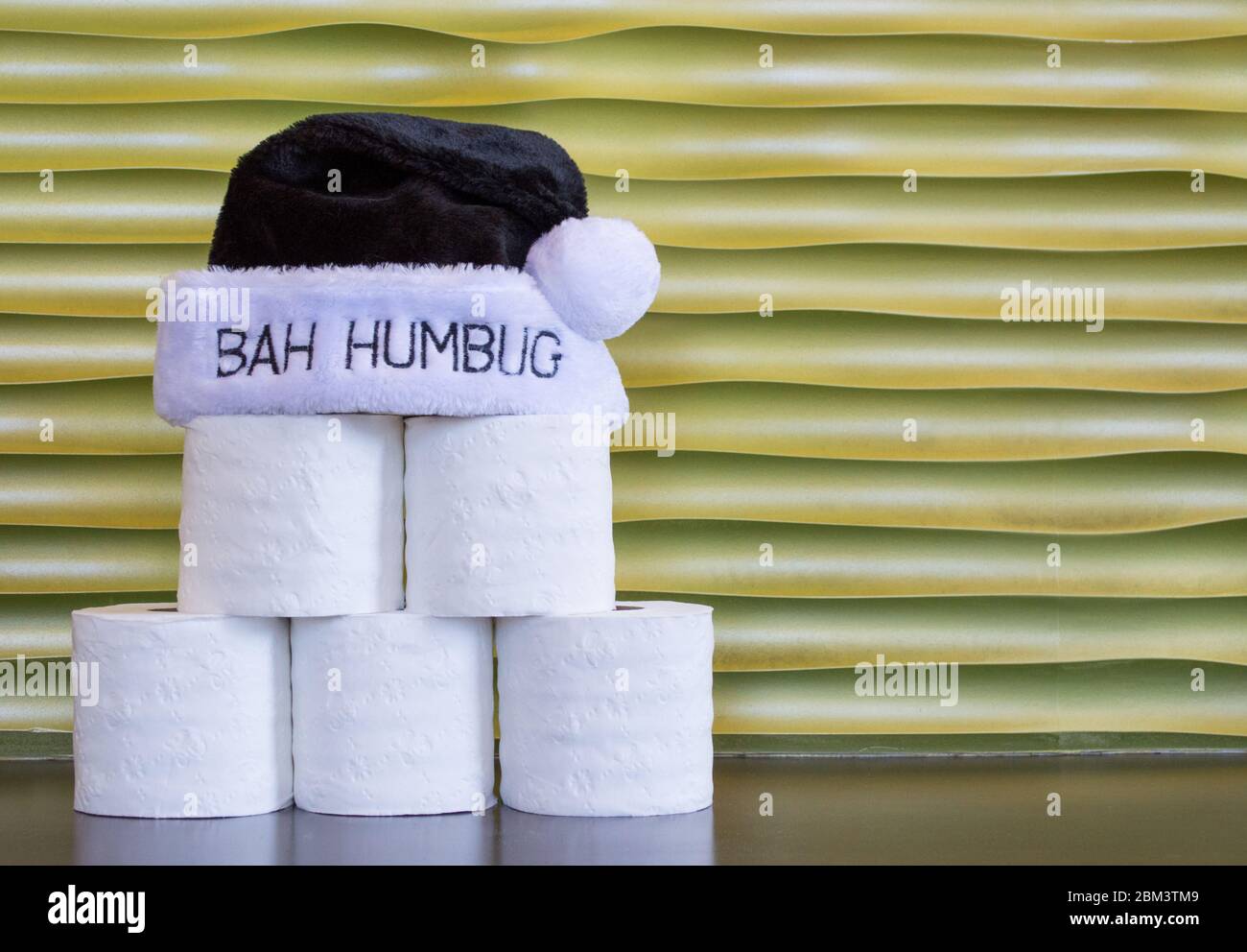 rolls of toilet paper stacked in a pyramid shape with a black and white Bah Humbug hat on top, against a gold background with copy space Stock Photo