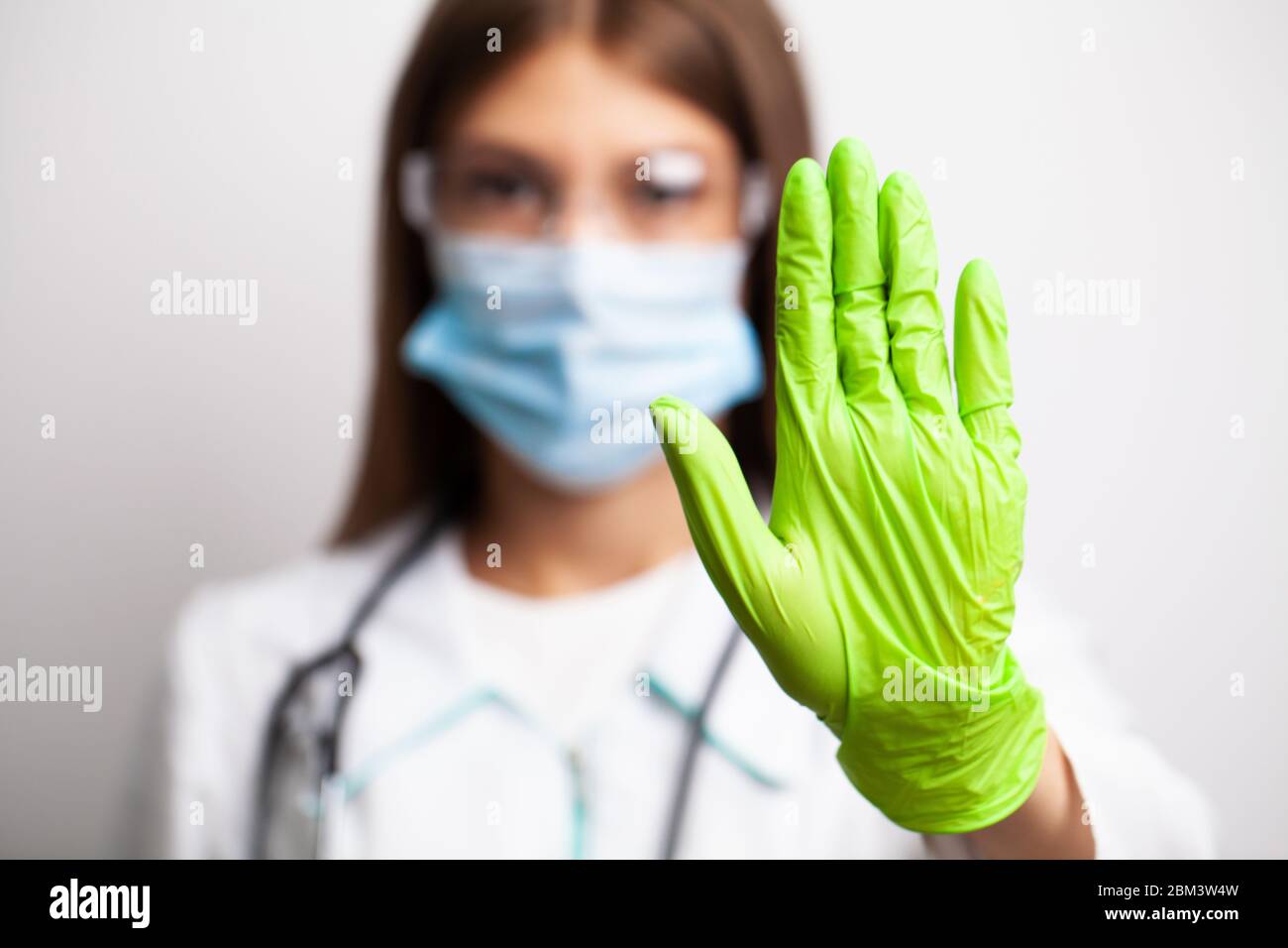 Doctor in white coat and green sterile gloves shows stop Stock Photo