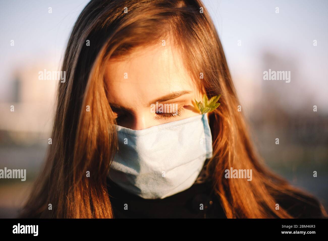 Close up portrait of sad teenage girl wearing protective face medical mask standing outdoors on city street Stock Photo