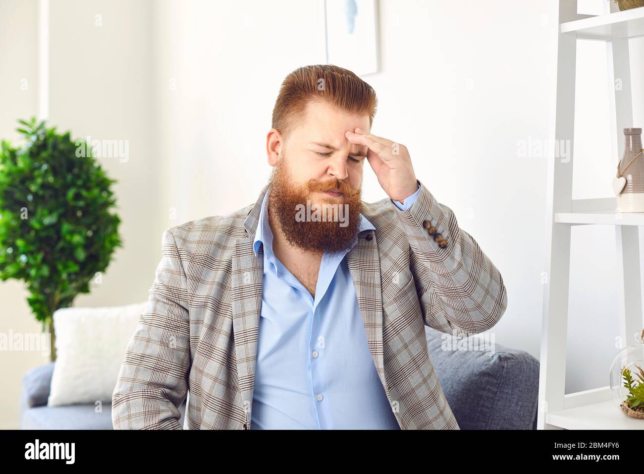 A man with a beard with a headache. Stress problems depression chronic pain. Stock Photo