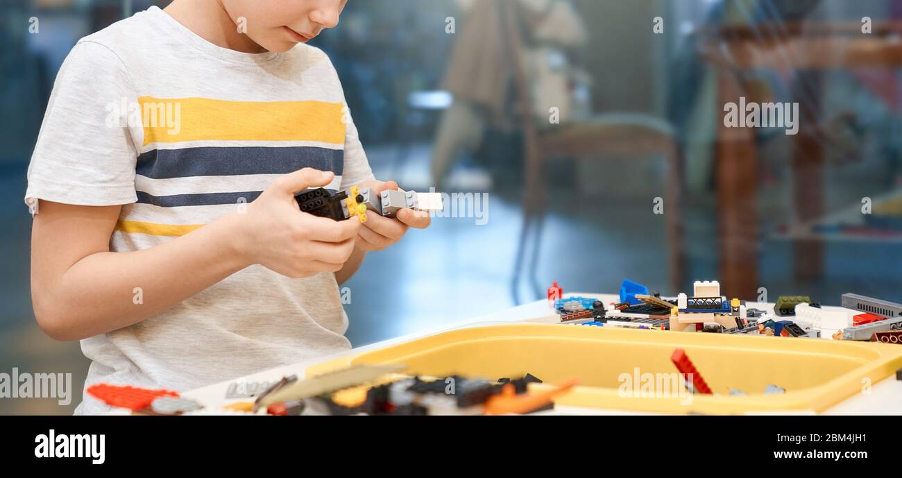 Selective focus of hands using building kit for kids, creating toys. Crop of incognito caucasian child working on project, taking colorful parts. Concept of science engineering. Stock Photo
