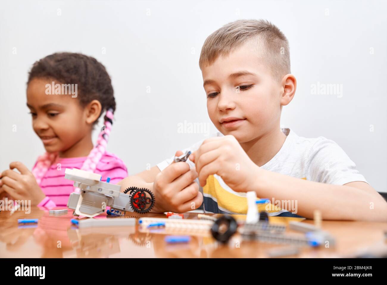 Front view of building kit for group of multiracial kids creating toys, having positive emotions and joy. Selective focus of lovely caucasian boy working on project, taking colorful parts. Stock Photo