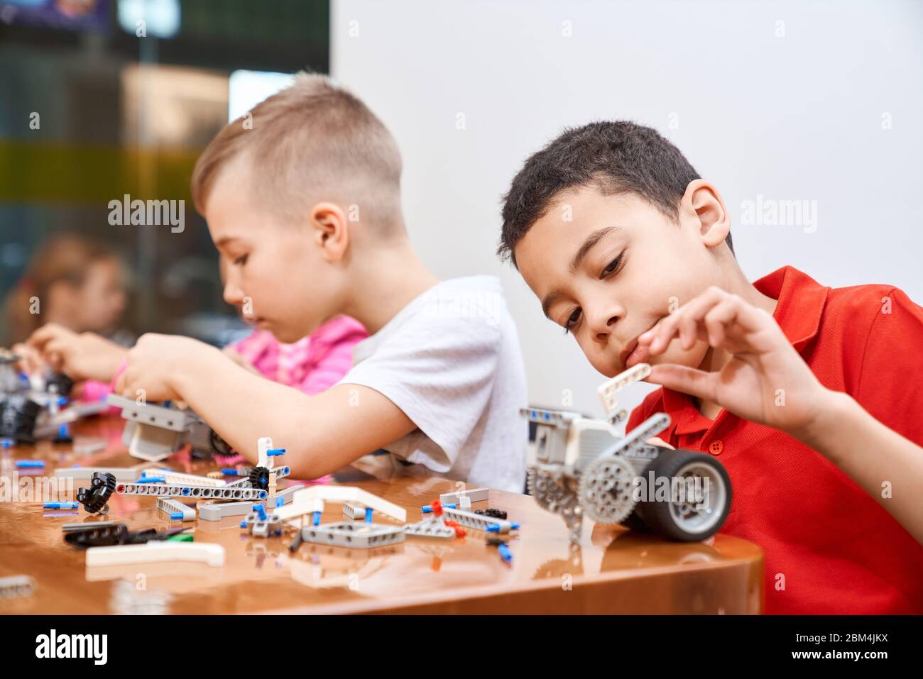 Side view of building kit with colorful pieces in box for group of multiracial kids creating robots, having positive emotions and joy. Close up of interested friends working on project. Stock Photo