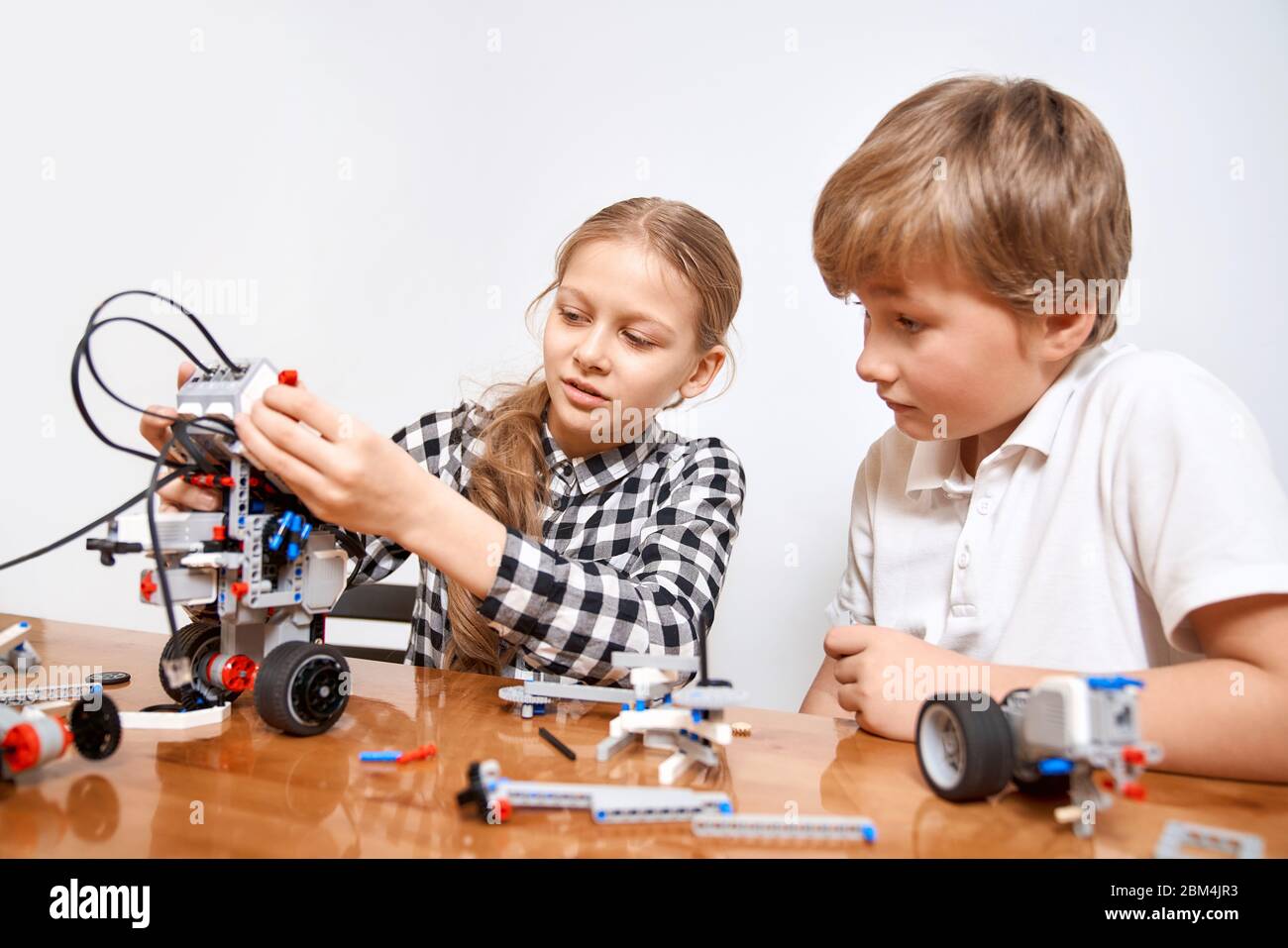 Front view of boy helping girl in creating robot using building kit for kids on table. Nice interested friends smiling, chatting and working on project together. Concept of science engineering. Stock Photo