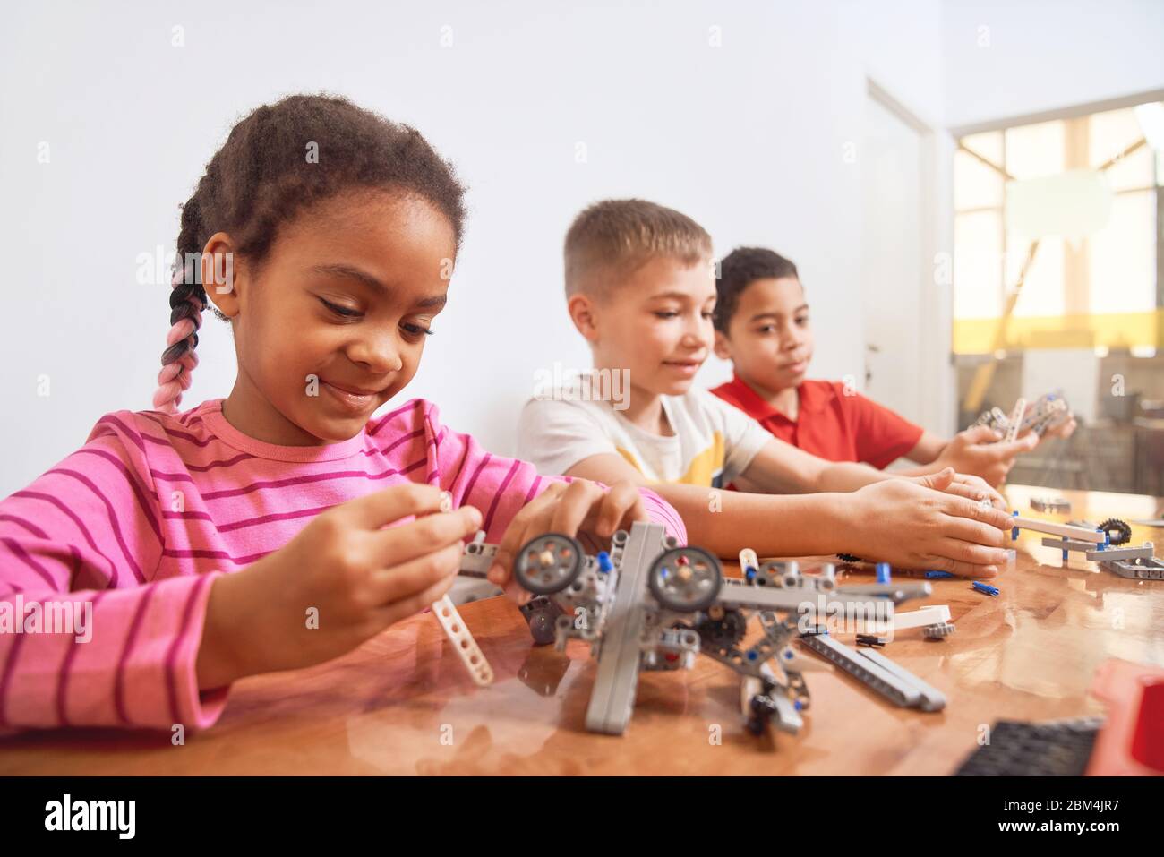 Building kit with colorful pieces for group of three multiracial kids creating toys, having positive emotions. Close up of smiling african girl working on project. Concept of science engineering. Stock Photo