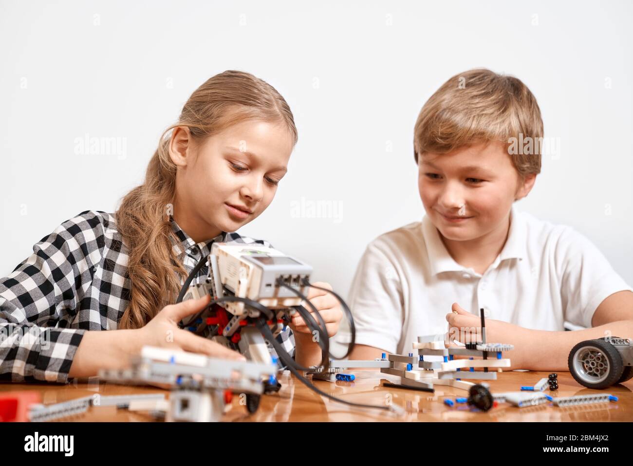 Front view of boy and girl having fun, creating robot. Science engineering. Nice interested friends smiling, chatting and working on project together using interesting building kit for kids on table. Stock Photo