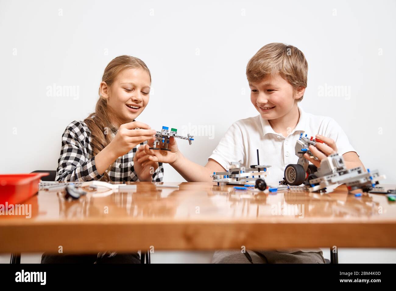 Interesting building kit for kids on table. Close up of boy and girl having fun at table, creating vehicles. Friends laughing, chatting and working on project together. Concept of science engineering. Stock Photo