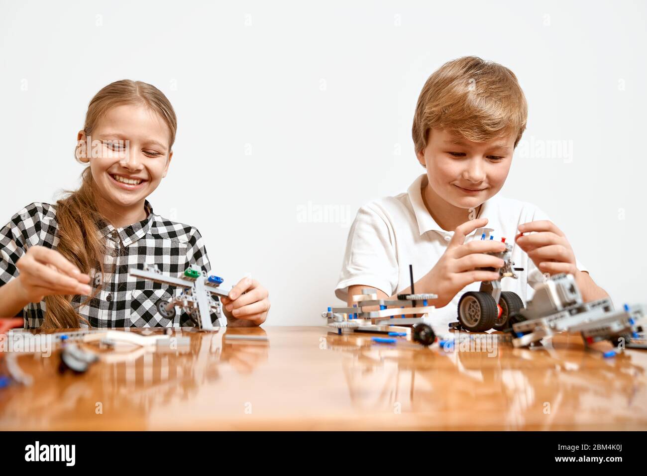 Interesting building kit for kids on table. Close up of boy and girl having fun at table, creating vehicles. Science engineering. Young friends laughing, chatting and working on project together. Stock Photo