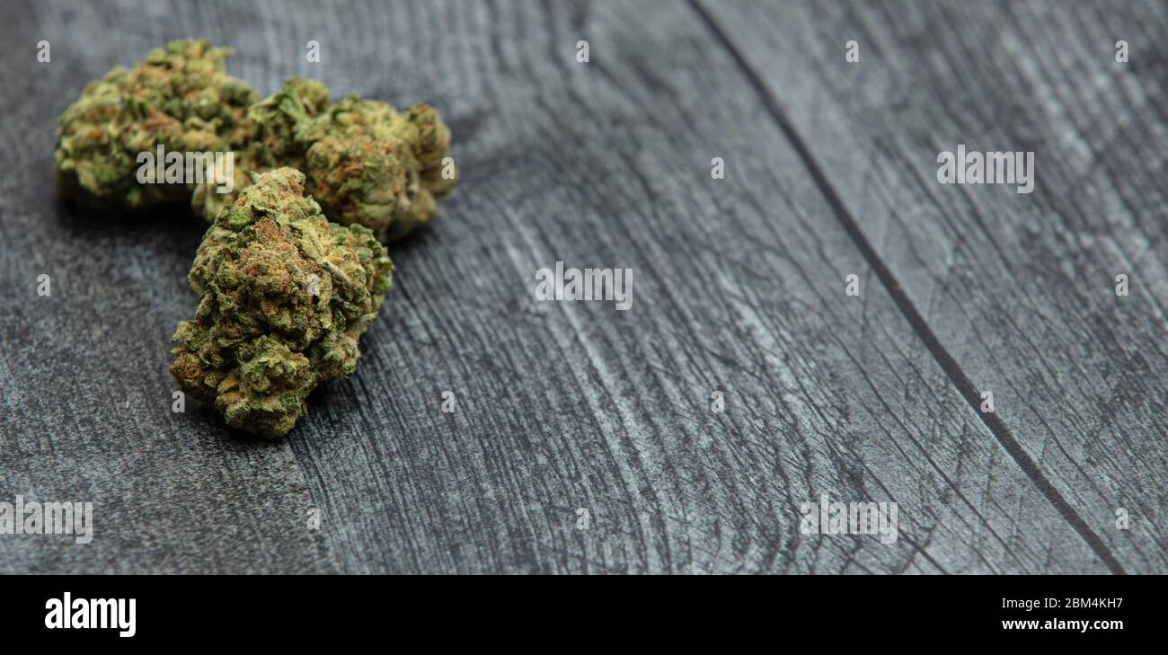 Three high quality bright green marijuana buds on a wooden table. Orange color and many crystals on buds. Stock Photo