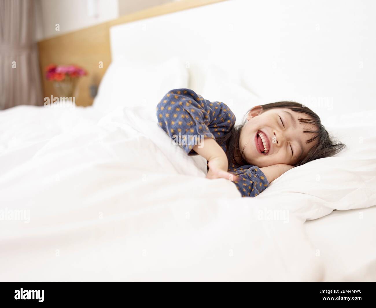 cute little asian elementary age girl lying in bed laughing while getting ready to sleep Stock Photo