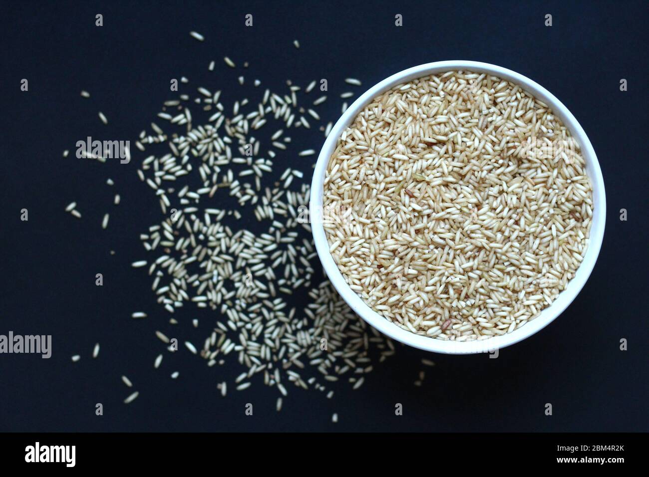 Brown rice grains in a white bowl on a dark background, seen from above Stock Photo