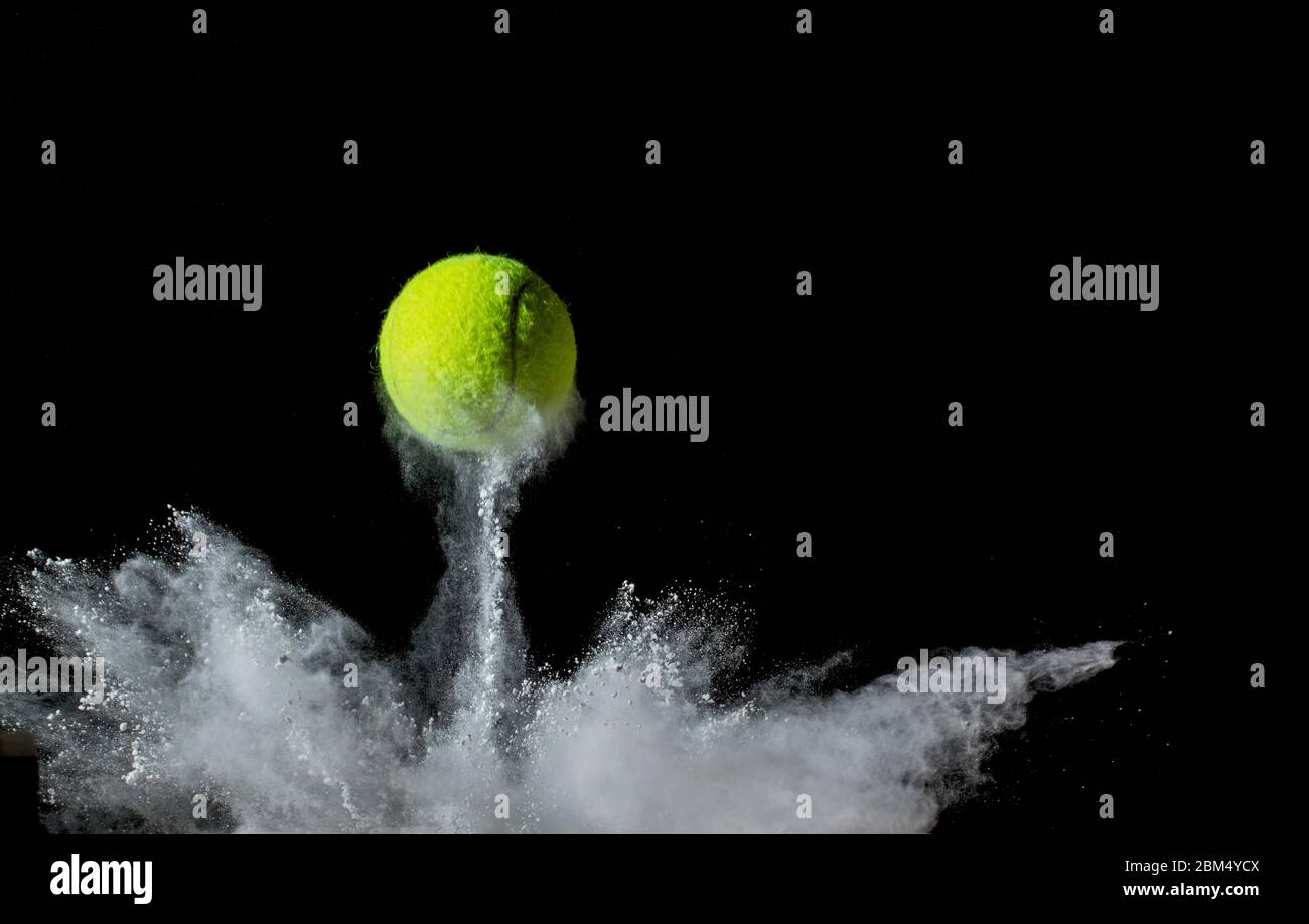 A tennis ball bouncing in chalk dust with black background. Conceptual