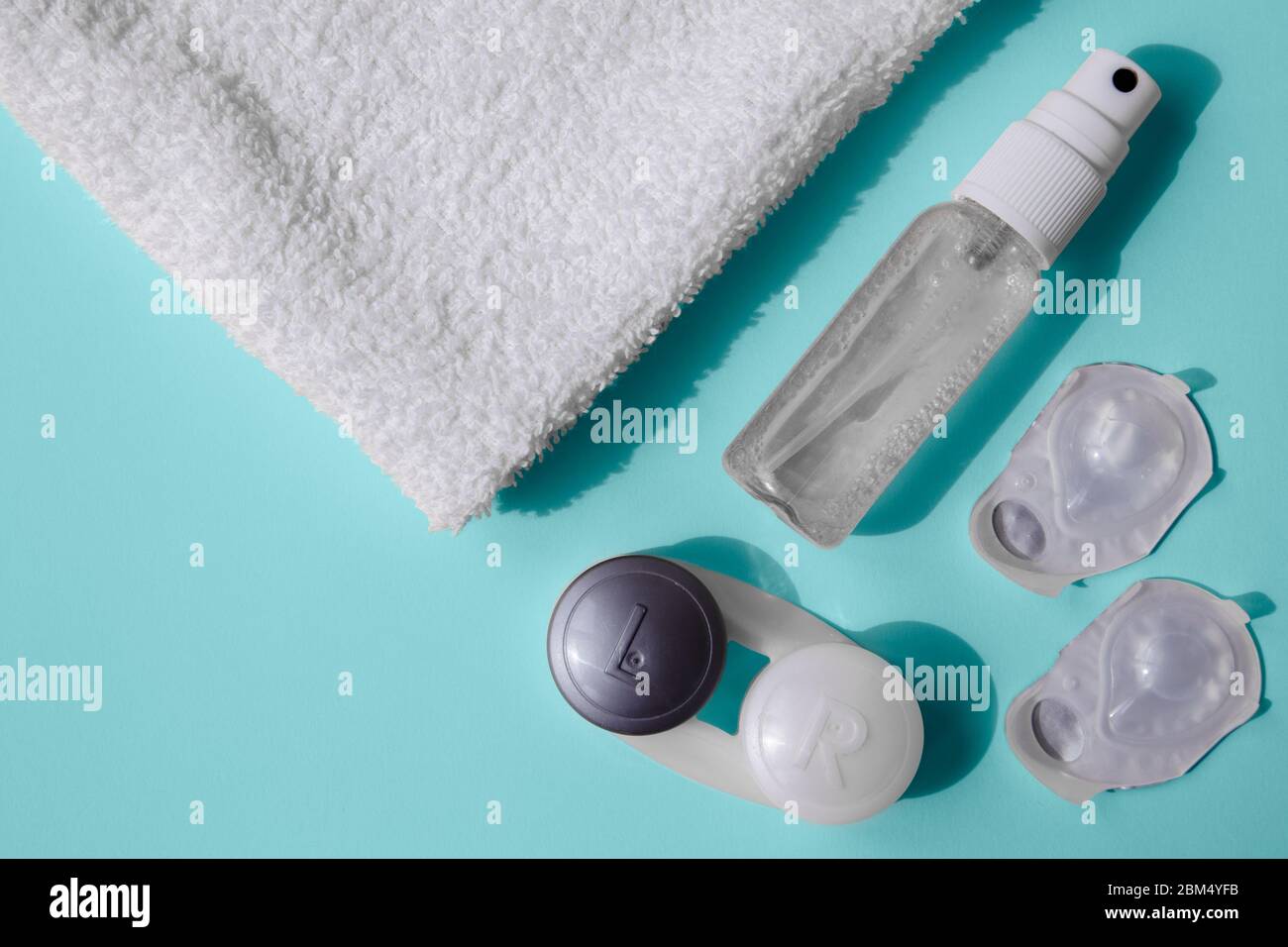 A set for using contact lenses. On a blue table are hand sanitizer, lens blisters, a lens container, and a white towel. Stock Photo