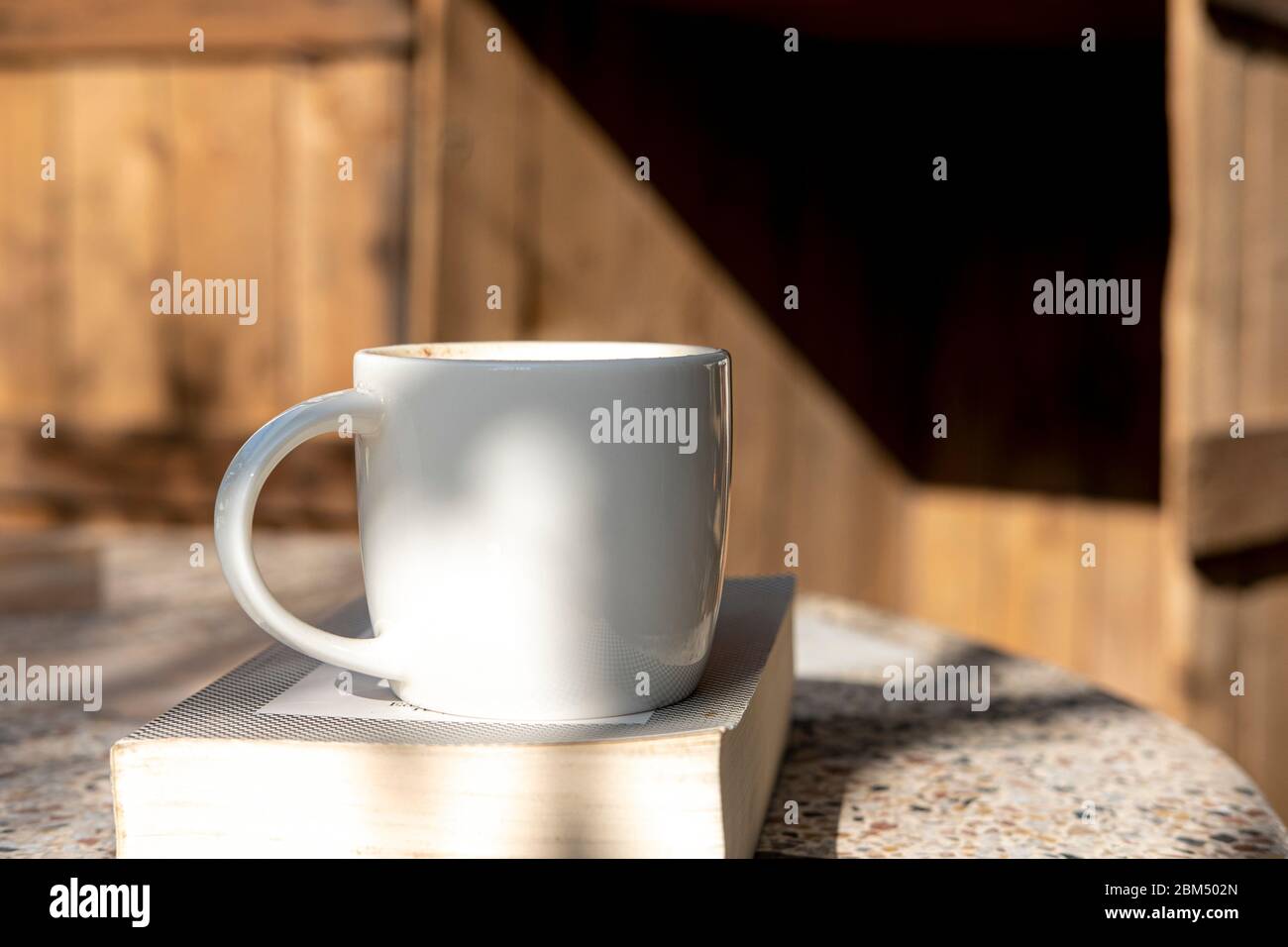 white cup with cappuccino coffee and books on an old table with a ...