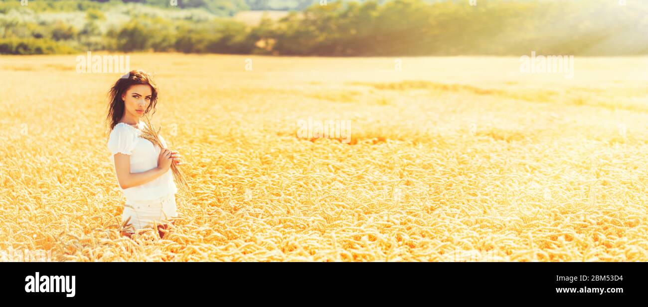 Beauty romantic girl enjoying nature in outdoors. Happy young woman in white shorts holding the ears on the field of golden ripe wheat in sun light. F Stock Photo