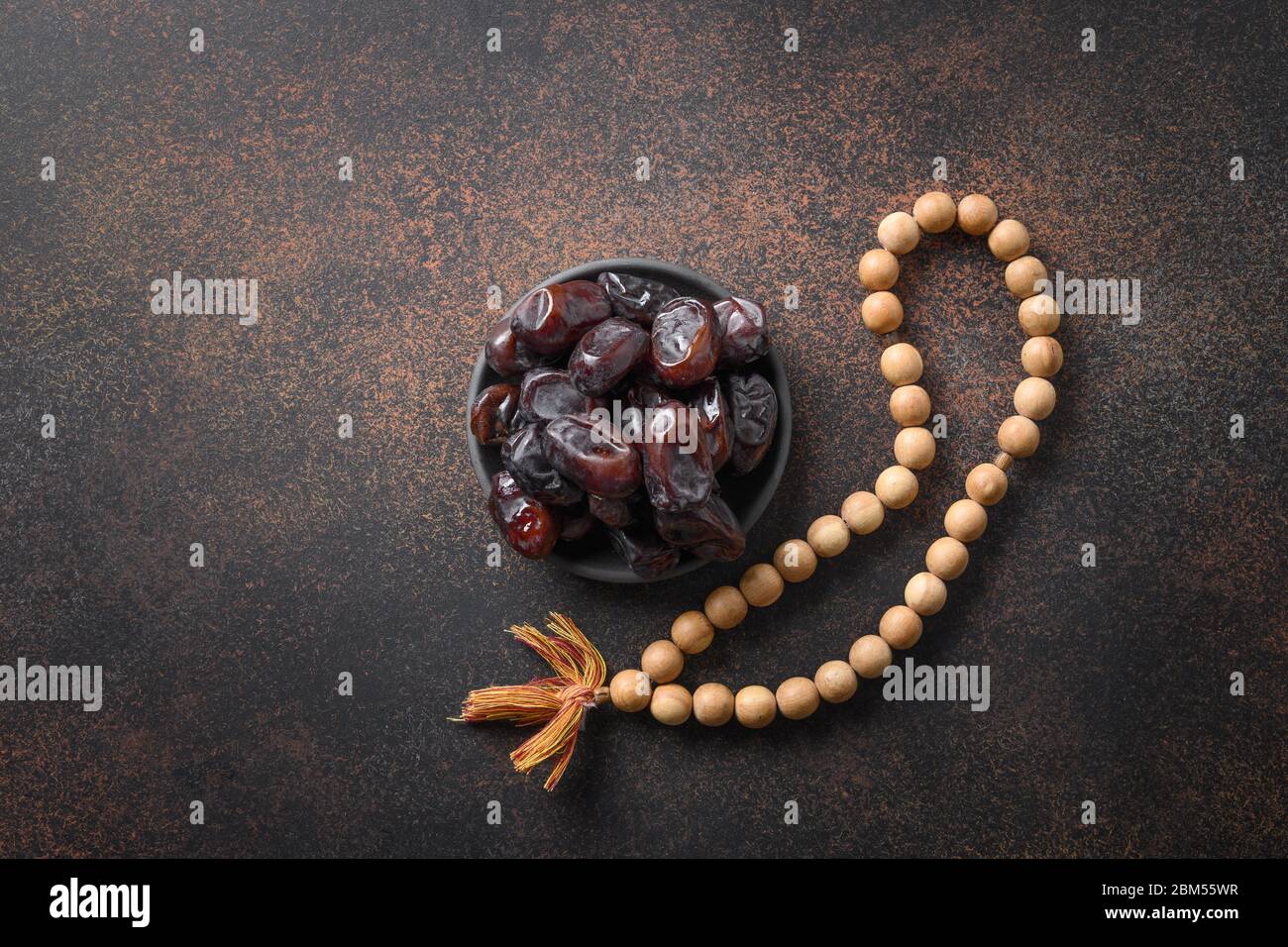 Ramadan. Wooden prayer beads and dates in bowl on brown. View from above. Eid Mubarak. Religious tradition. Stock Photo
