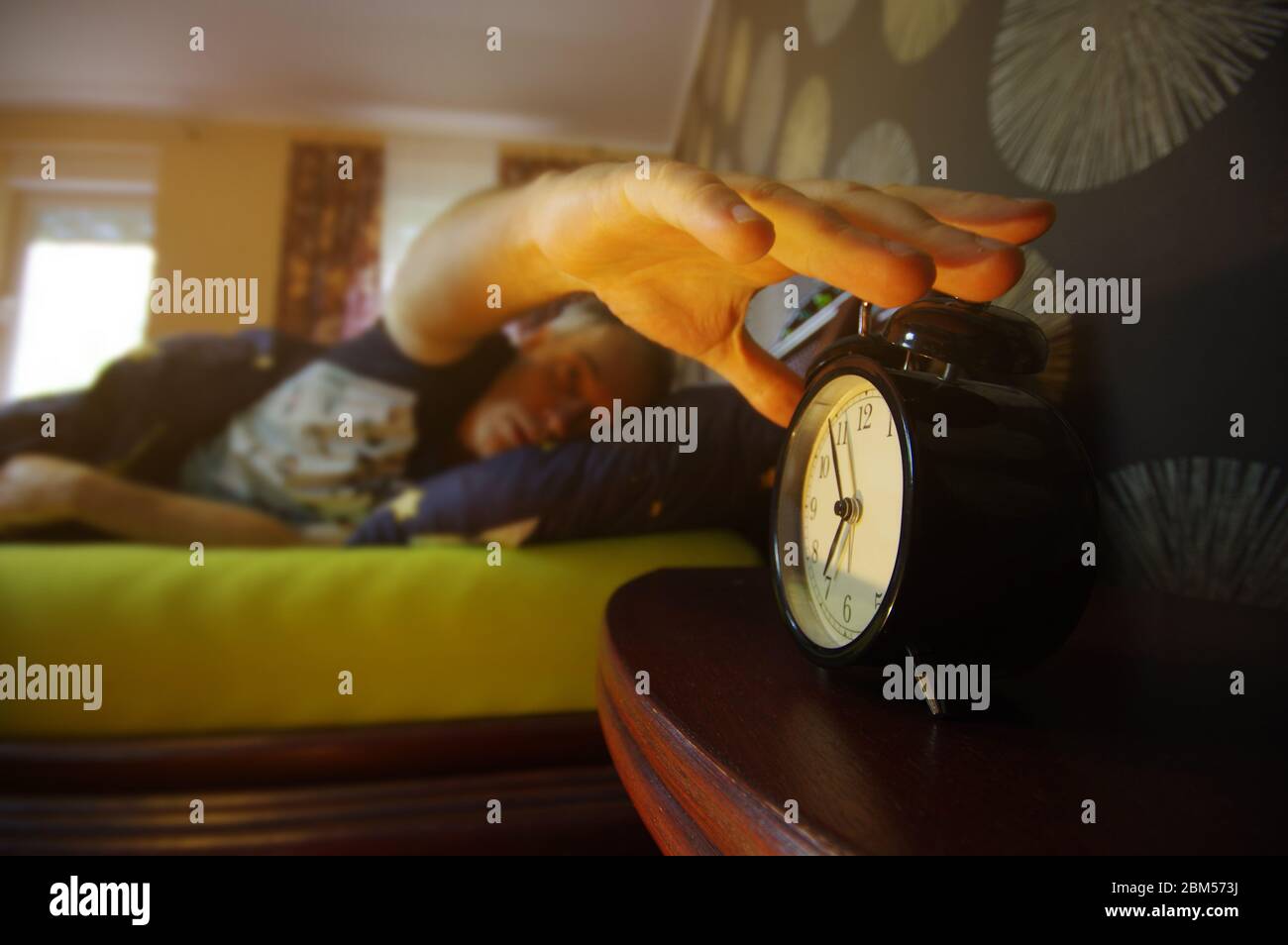 Morning wake up in the bedroom. The man turns off the alarm. Early clock time at the beginning of the day. Stock Photo