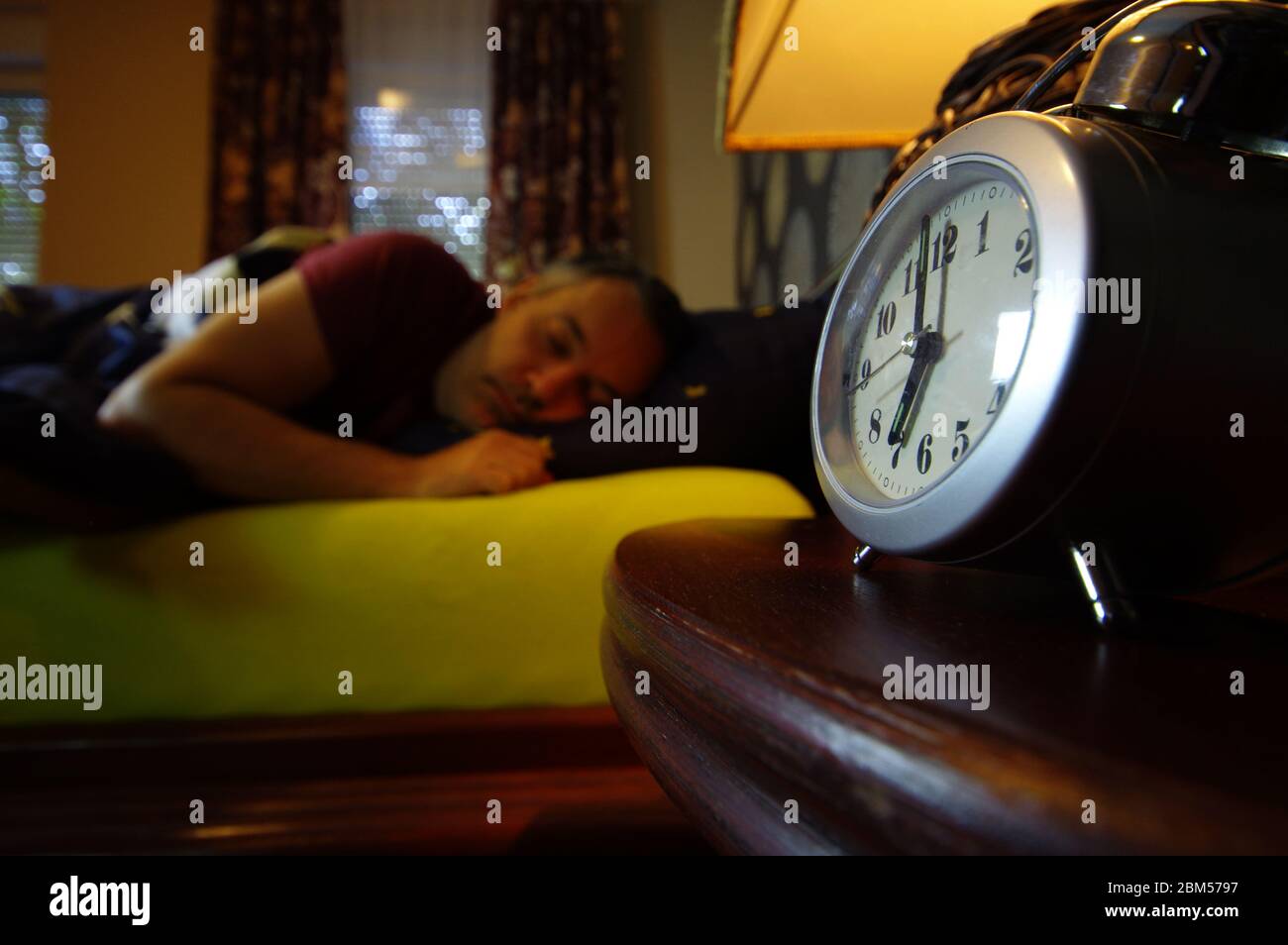 Morning wake up in the bedroom. The man turns off the alarm. Early clock time at the beginning of the day. Stock Photo