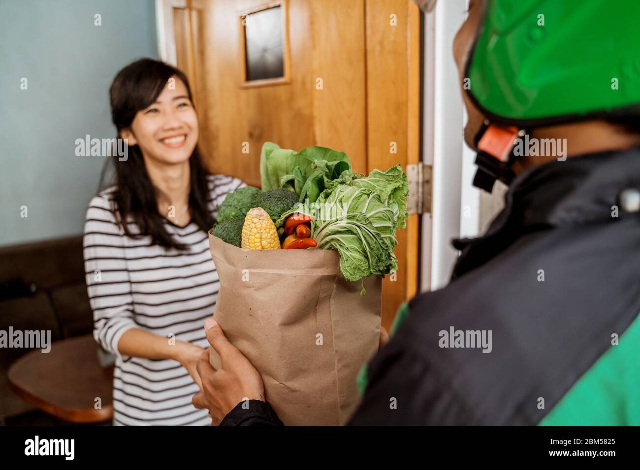 https://c8.alamy.com/comp/2BM5825/delivery-boy-is-delivering-some-groceries-to-woman-he-is-handing-her-a-shopping-bag-at-her-front-door-2BM5825.jpg