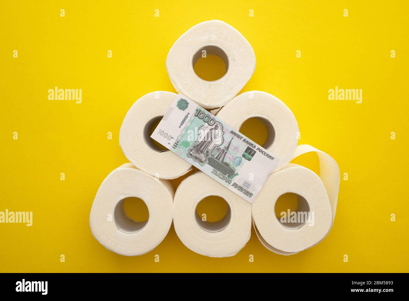 top view of white toilet paper rolls arranged in pyramid with russian money on yellow background Stock Photo