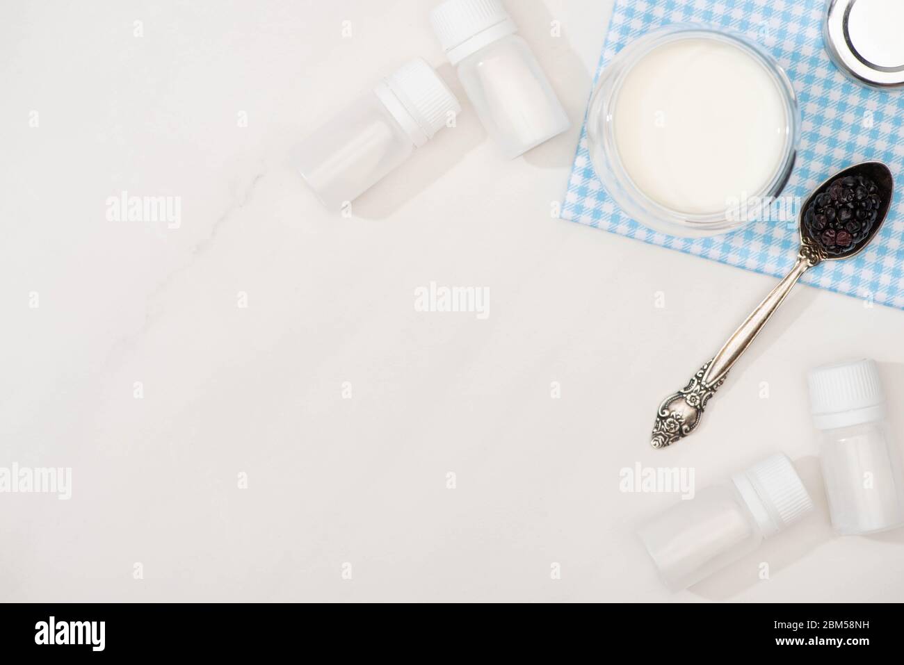 Top view of glass of yogurt and teaspoon with blackberry on cloth near