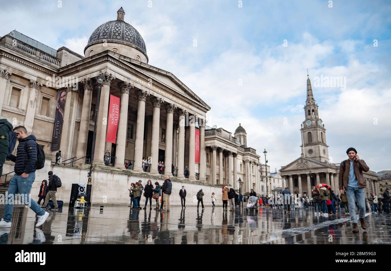 London Tourists. A wet view of Trafalgar Square dominated by The National Gallery and St. Martin-in-the-Fields Church. Stock Photo