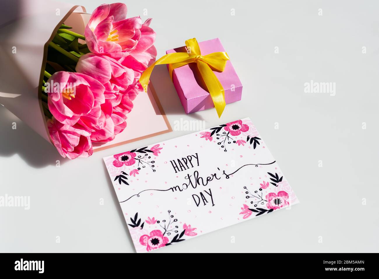 sunlight on pink tulips near gift box and greeting card with happy ...