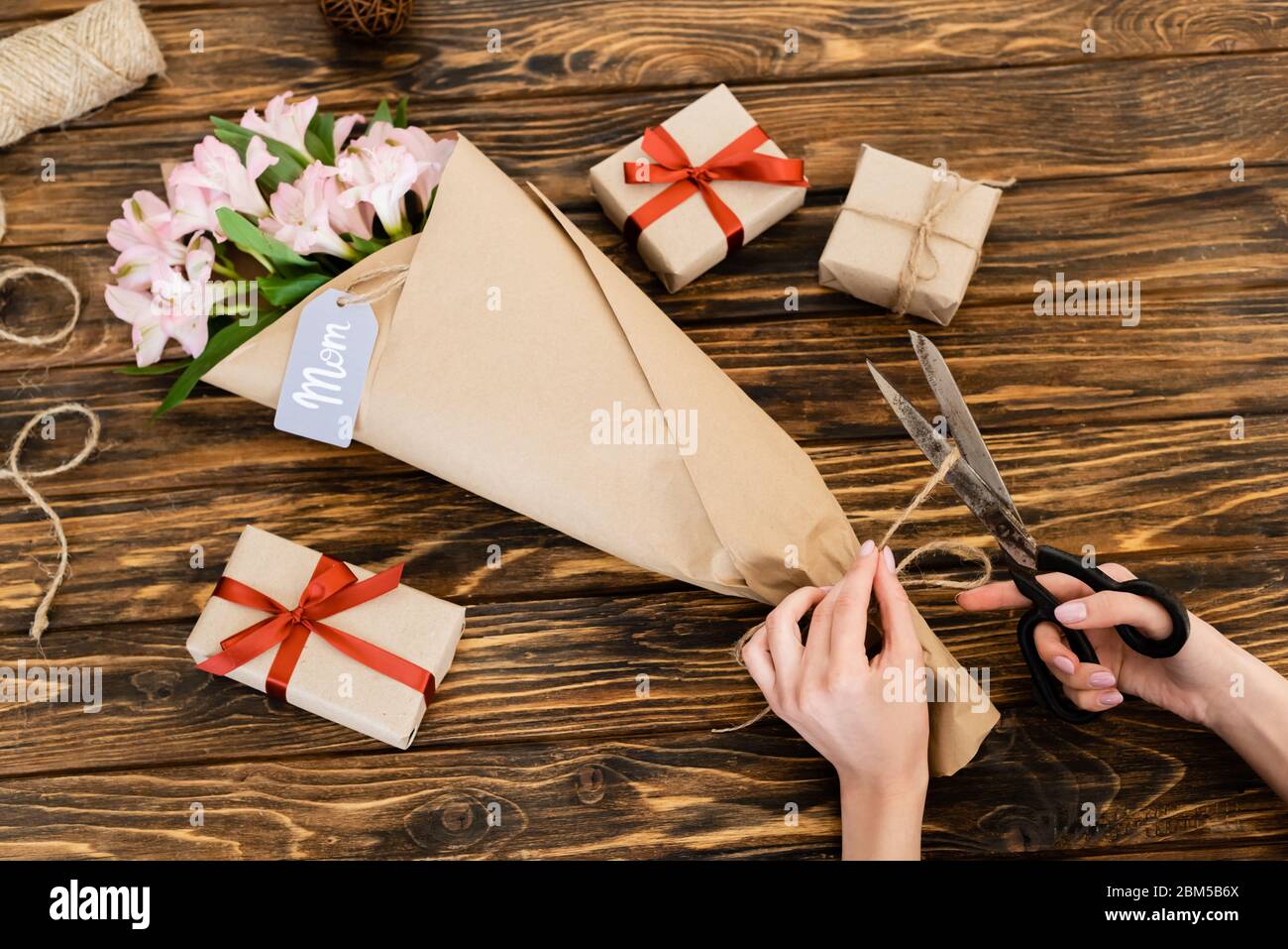 https://c8.alamy.com/comp/2BM5B6X/cropped-view-of-woman-cutting-jute-twine-rope-on-pink-flowers-wrapped-in-paper-near-gift-boxes-and-scissors-mothers-day-concept-2BM5B6X.jpg