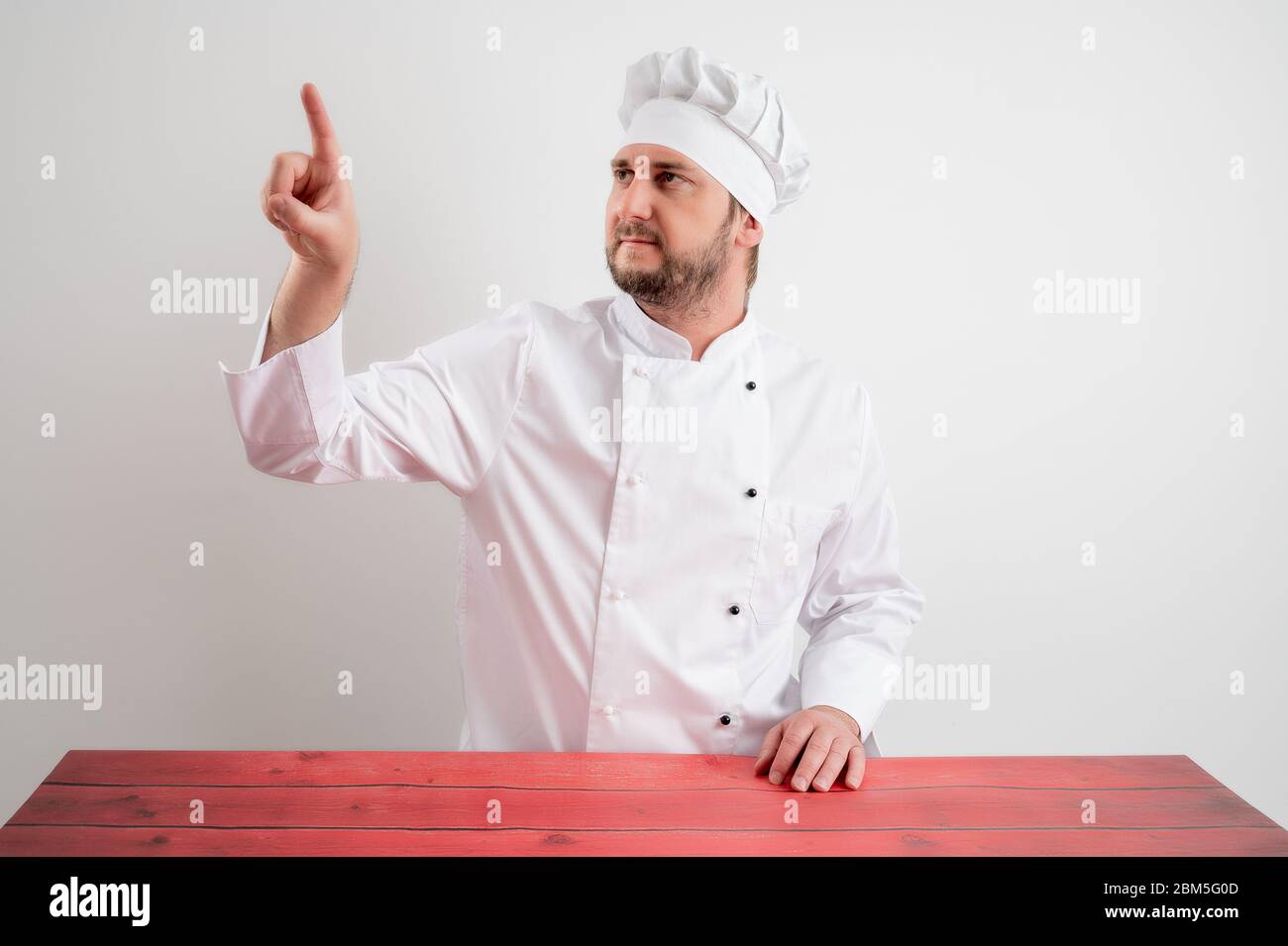 Young male chef in white uniform presses a virtual button posing on a white isolated background Stock Photo