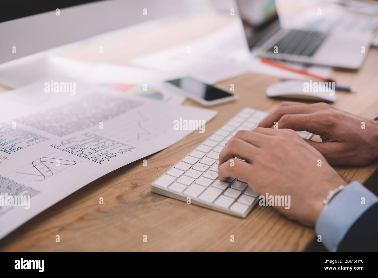 Cropped view of data analyst using computer keyboard near papers with graphs on table Stock Photo