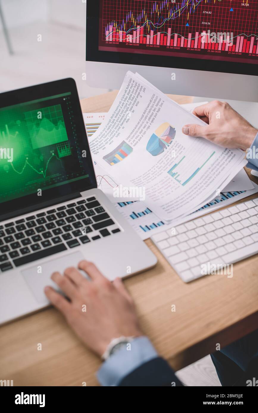 Cropped view of data analyst using laptop and papers with graphs while testing security of computer systems Stock Photo