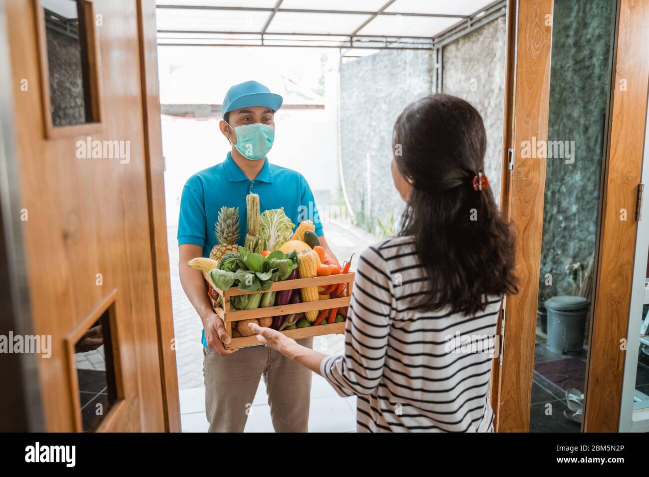 Food delivery during corona virus pandemic. Courier wearing face masks delivering grocery to customer at home. online shopping order during social distancing Stock Photo