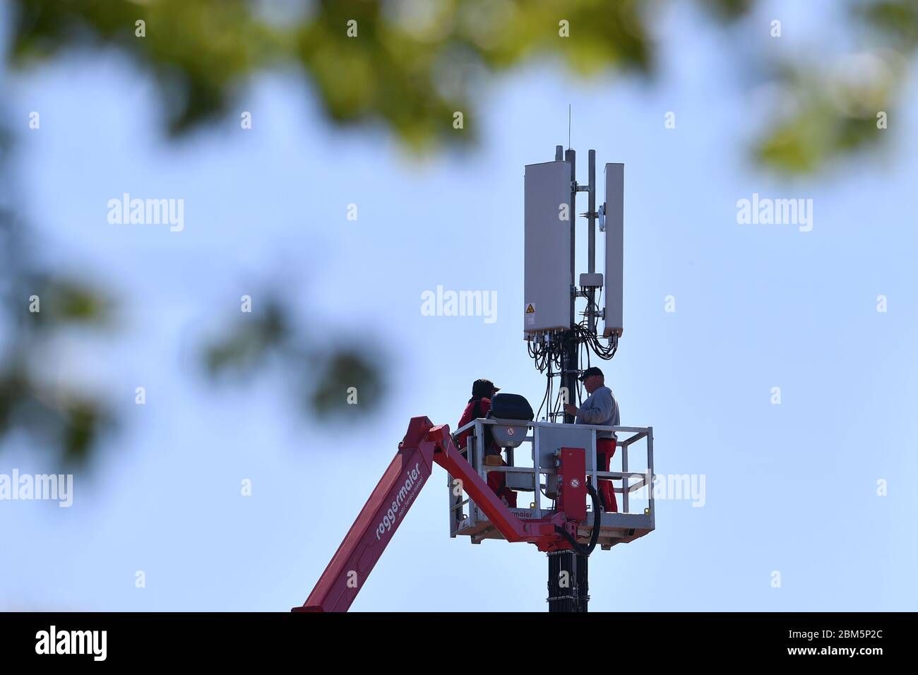 Cell phone mast on a house roof. Workers stand on a lifting platform