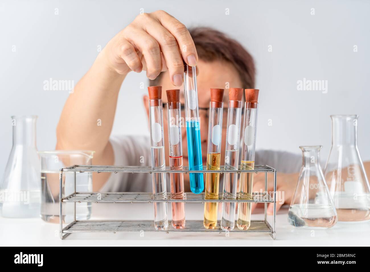 A man lifting up test tube with blue liquid from the rack, education or science experimental concept Stock Photo