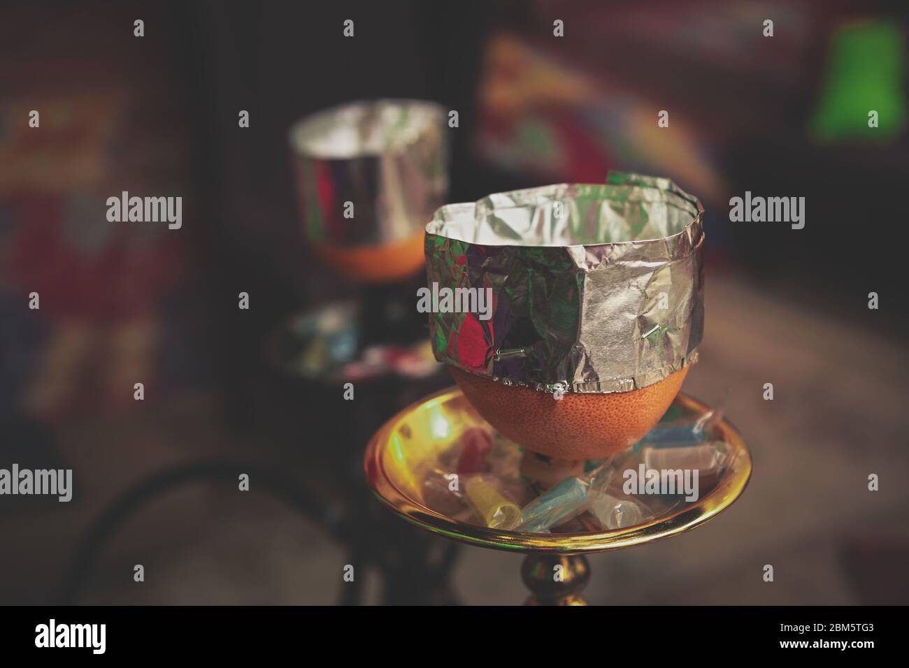 Hookah with flavored tobacco on orange fruit bowl covered with foil to
