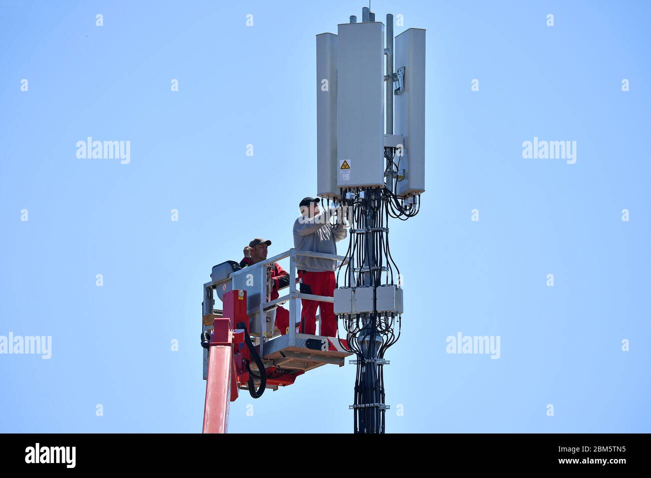 Cell phone mast on a house roof. Workers stand on a lifting platform