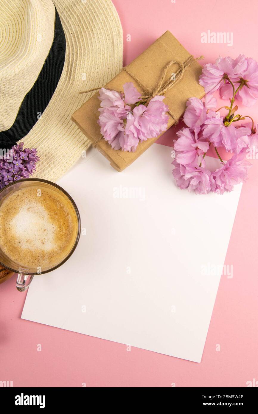Empty paper on clipboard, summer mock-up. An empty sheet of paper surrounded by a beach hat, pink flowers, coffe and macaroons stands on a pink Stock Photo
