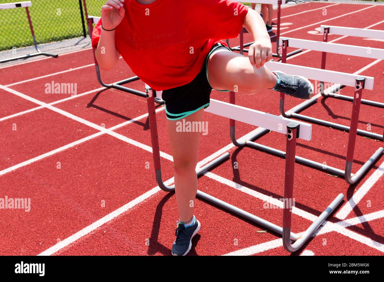 A female high school runner is doing hurdle drills on a red track