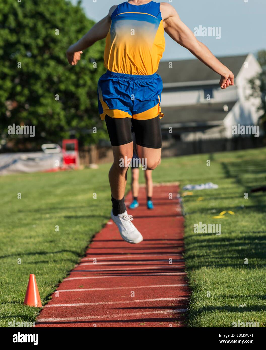 A teenage boy is flying in the air getting ready to land in the sand pit during a triple jump competition at a track and field event. Stock Photo