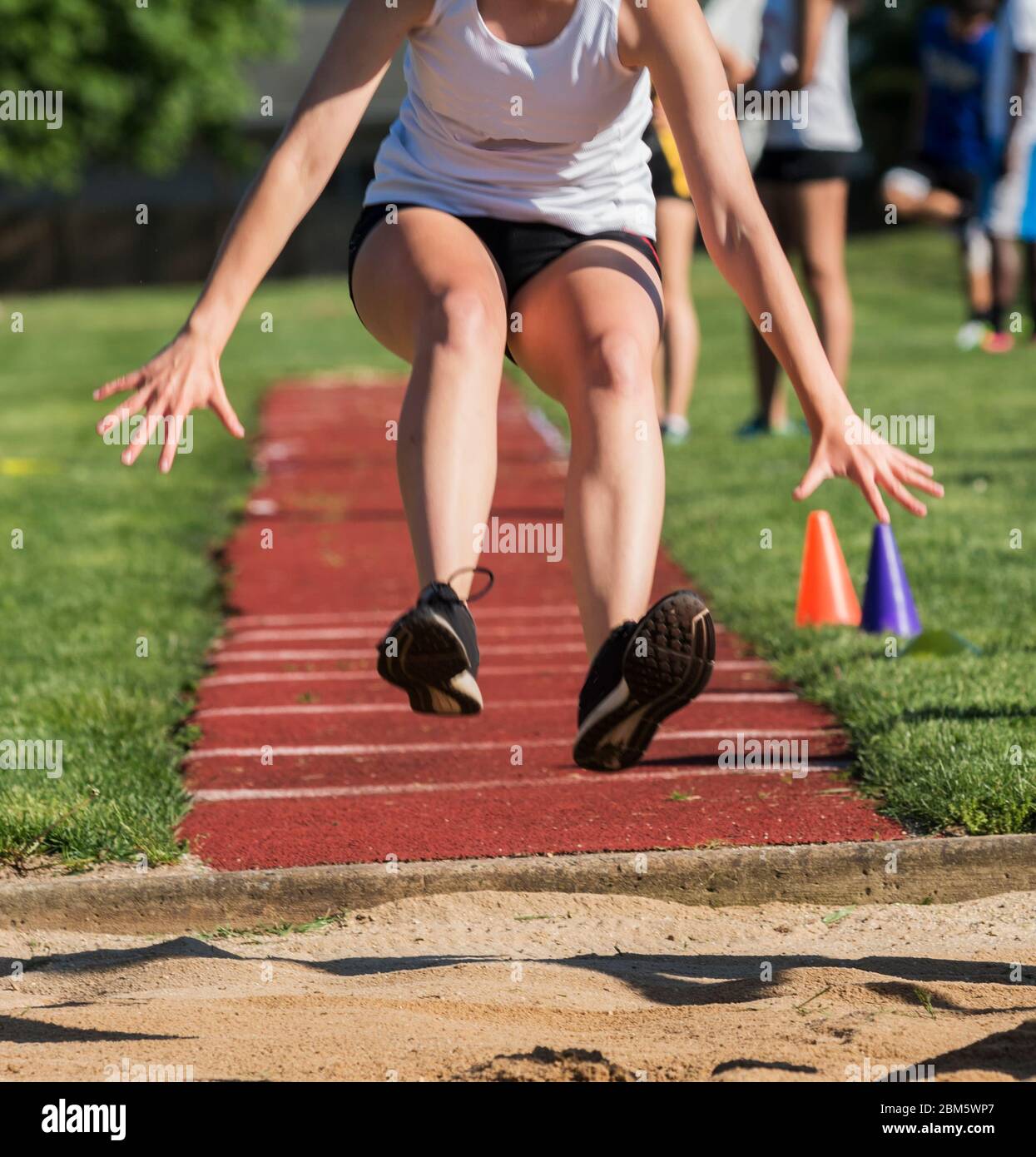 A high school teenage girl is competitin in the triple jump diring a track and field competition and is landing into the sane pit. Stock Photo