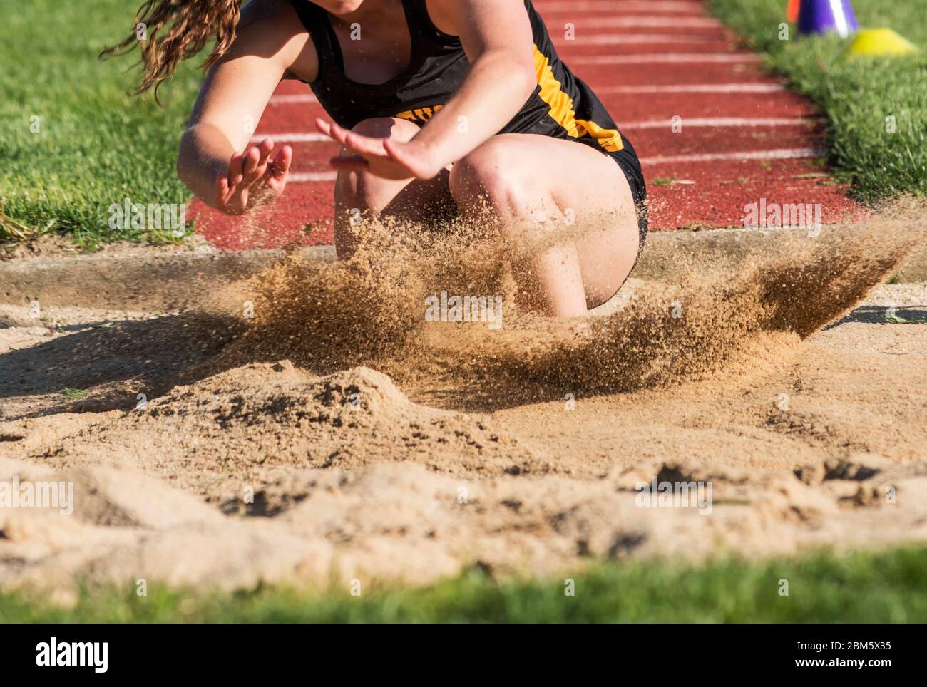 Close up of a young female high school long and triple jumper landing violently in the sand during a competition. Stock Photo