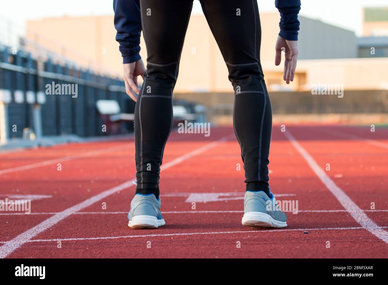 A runner in black spandex gets ready to sprint down a red track Stock Photo