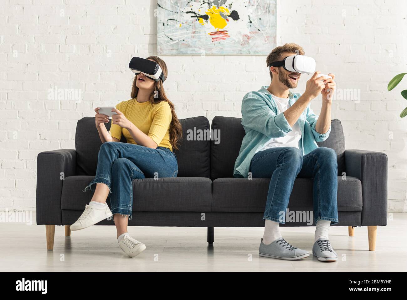 Couple using virtual reality headsets and smartphones on couch Stock ...